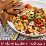 Overhead view of a bowl of fattoush salad with serving utensils.