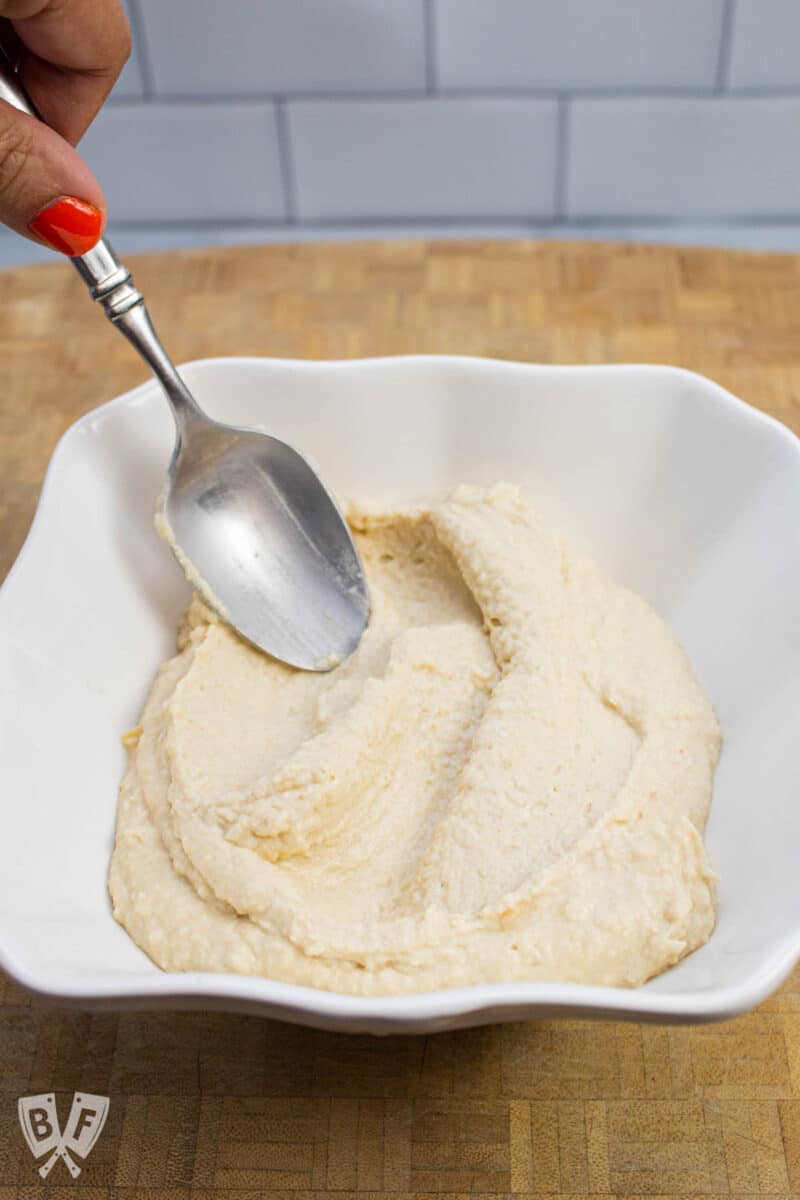 Smoothing hummus into a bowl with a spoon.