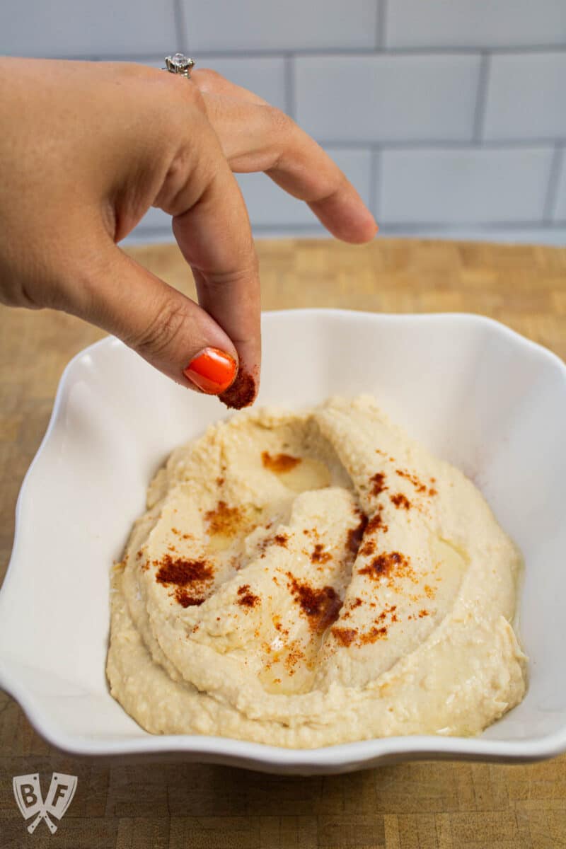 Sprinkling paprika onto a bowl of hummus.