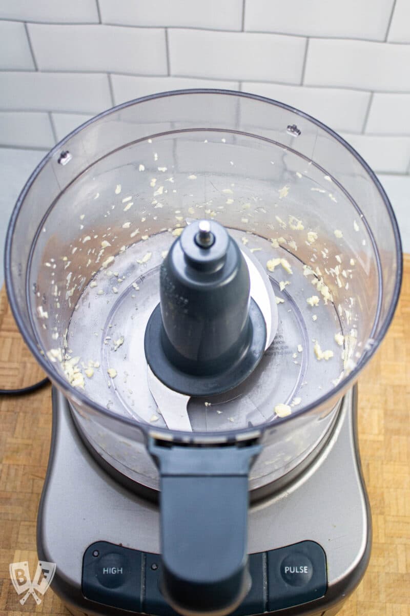 Overhead view of a food processor containing minced garlic.