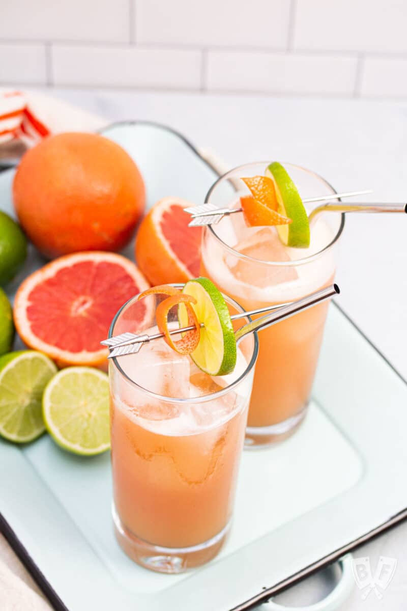 Overhead view of 2 guava tequila cocktails on a tray with fresh citrus fruit.