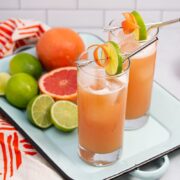 Guava cocktails on a tray with fresh citrus fruit in the background.