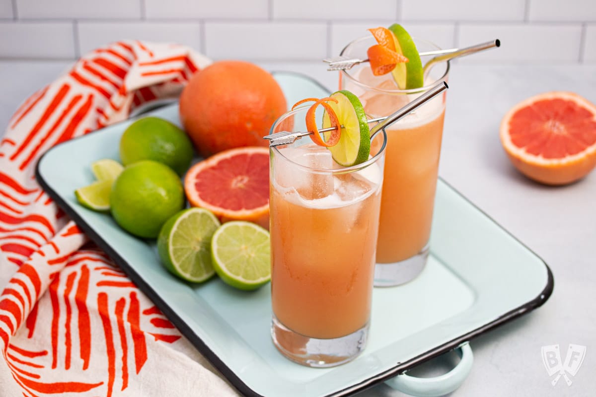 Guava cocktails on a tray with fresh citrus fruit in the background.