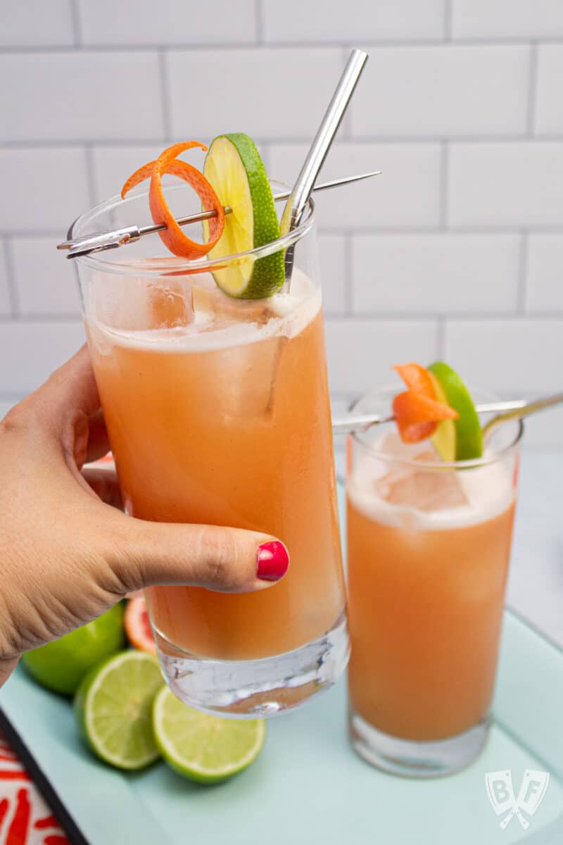 Holding a guava cocktail glass garnished with lime and grapefruit.