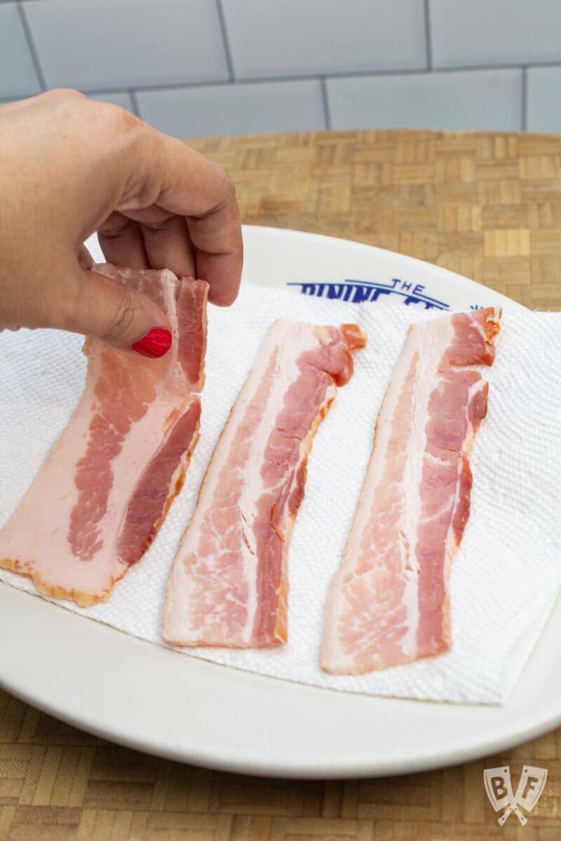 Placing thick-cut bacon on a paper towel-lined plate.