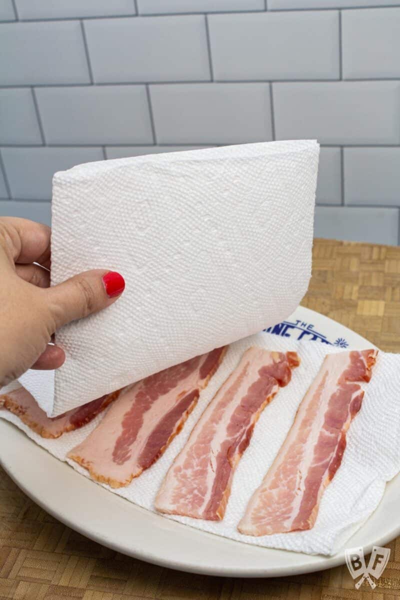 Covering bacon with paper towels on a plate.