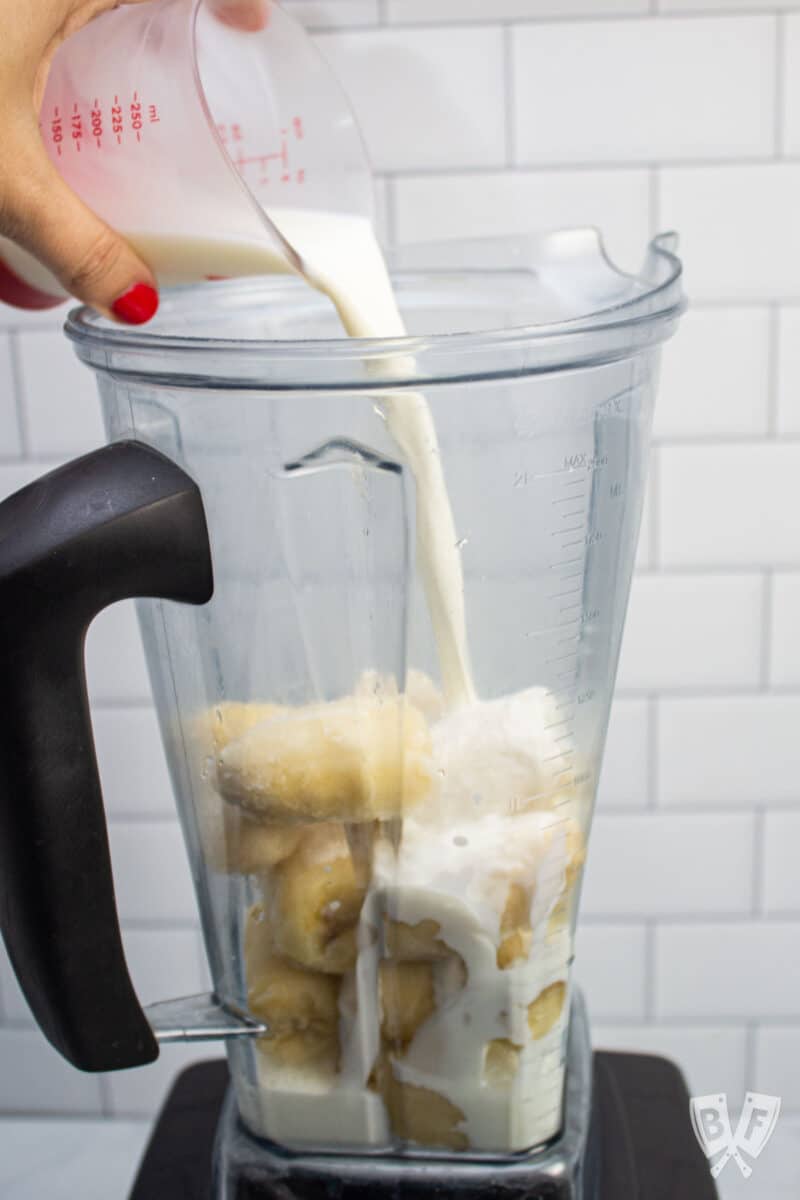 Pouring milk into a blender with frozen bananas.