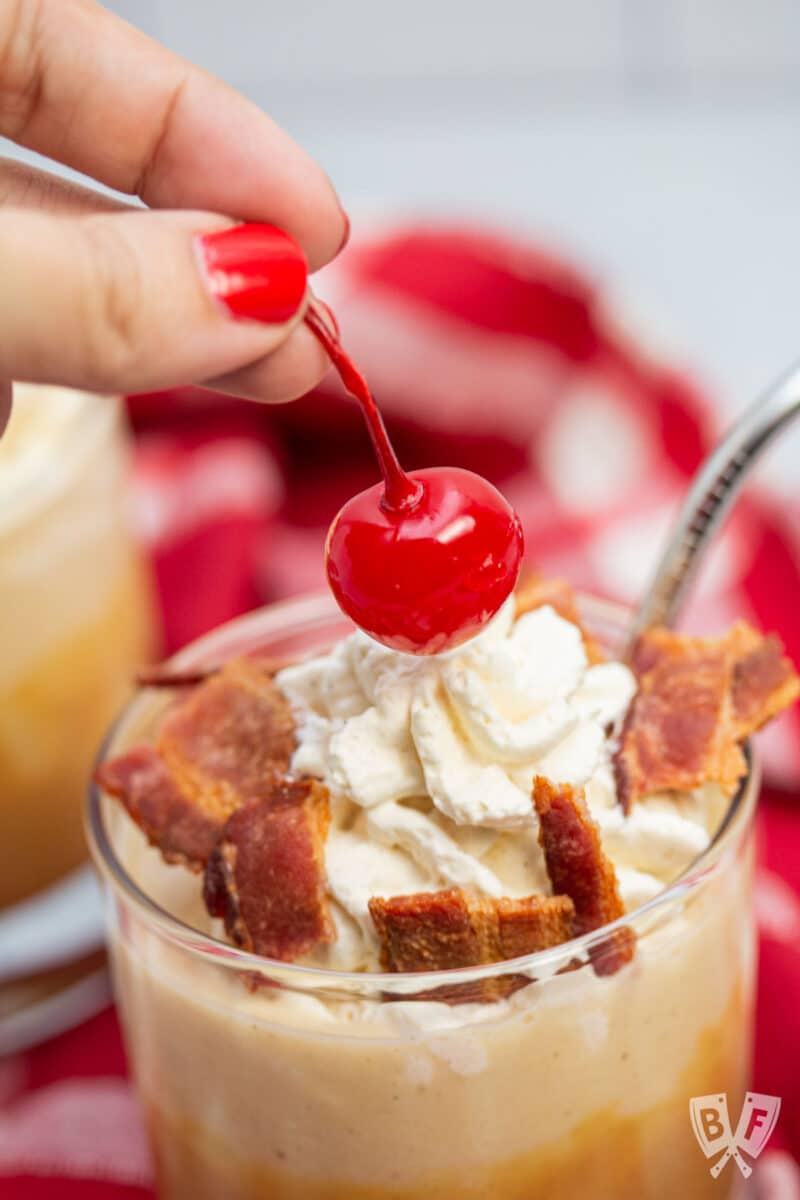 Topping a peanut butter banana milkshake with bacon and a maraschino cherry.