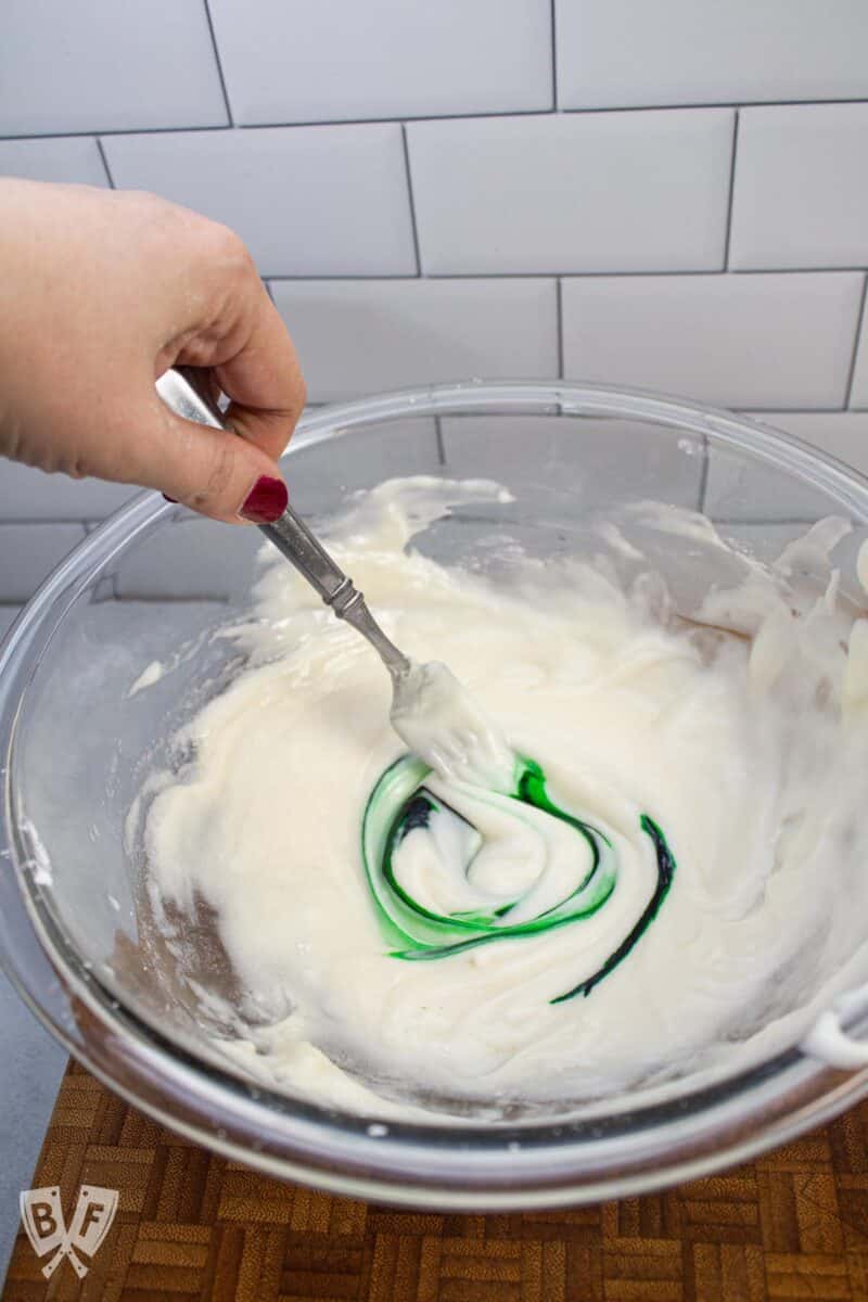 Mixing green food coloring into a bowl of icing.