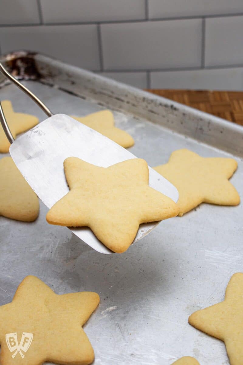 Metal spatula lifting a star-shaped sugar cookie off of a baking sheet.