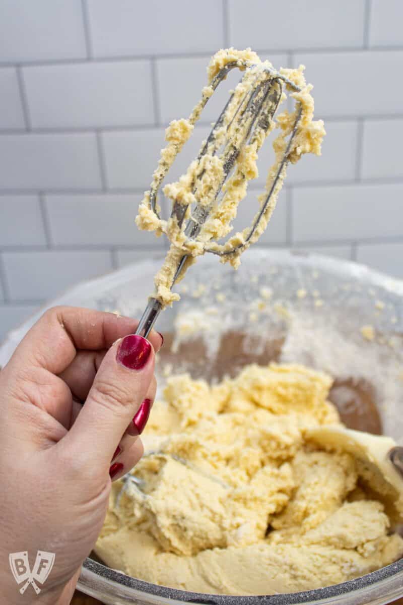 Holding a beater from an electric mixer in front of a bowl of cookie dough.