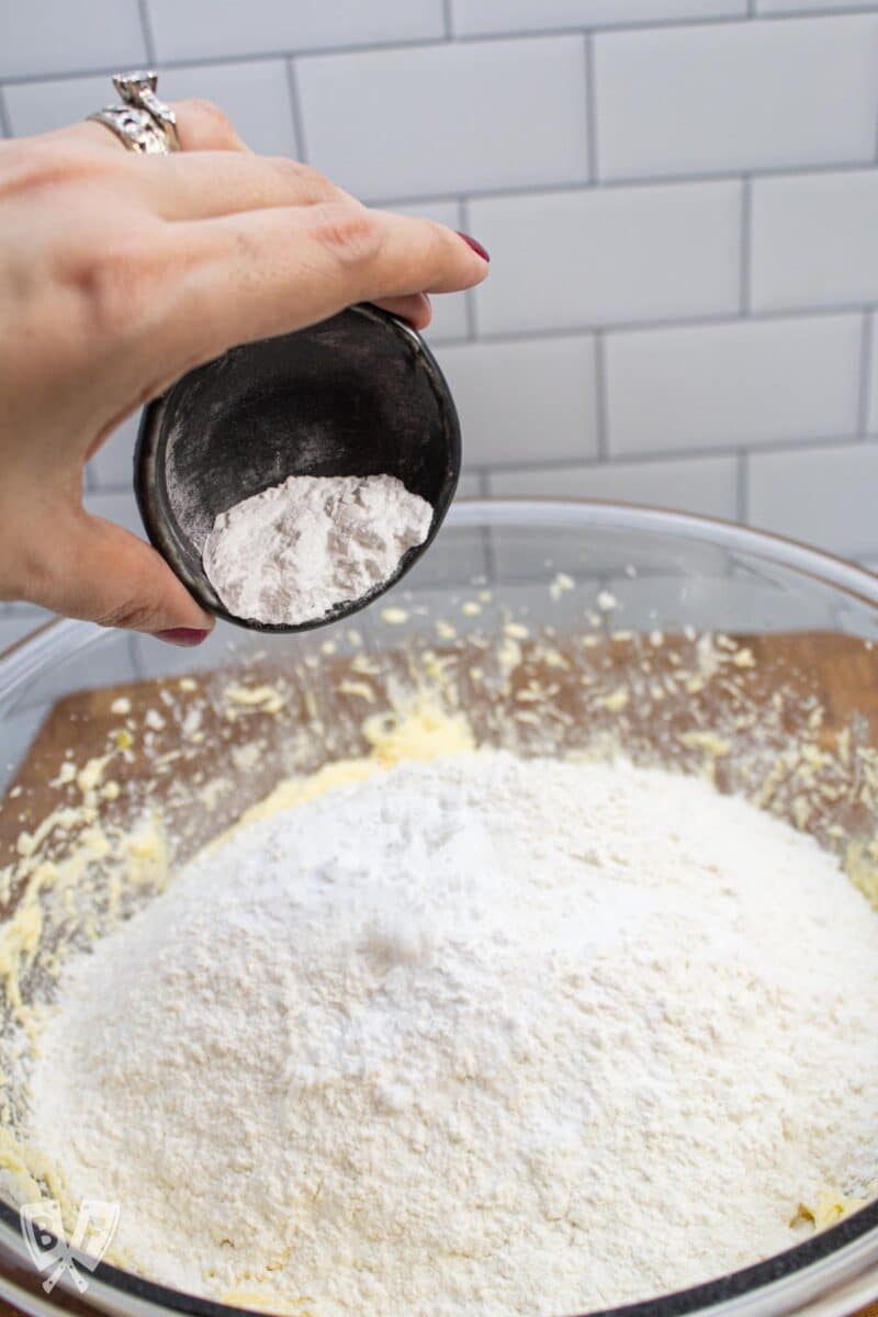 Adding cream of tartar to a bowl of sugar cookie ingredients.