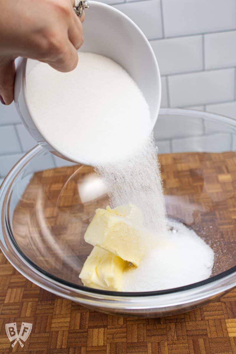 Pouring sugar into a bowl with softened butter.