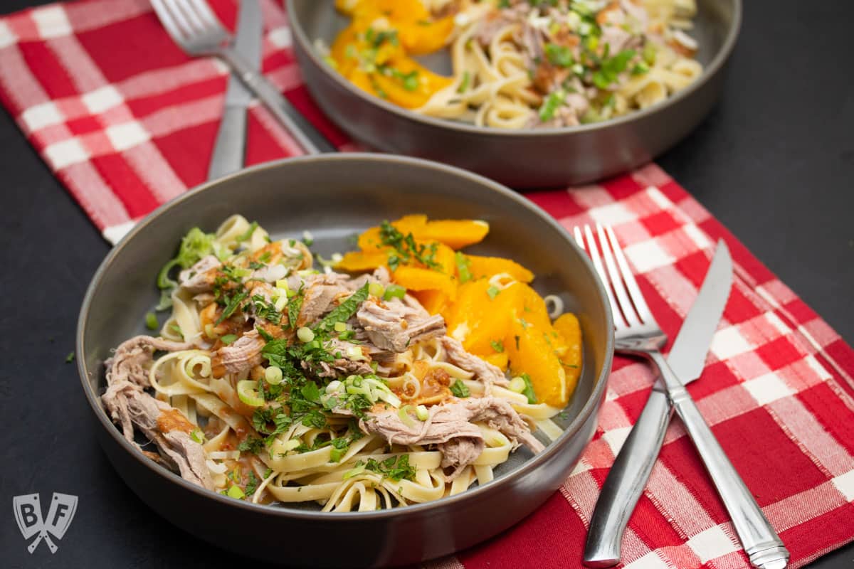 2 Bowls of peanutty noodles with roasted pork and honeyed oranges with fresh herbs on top.