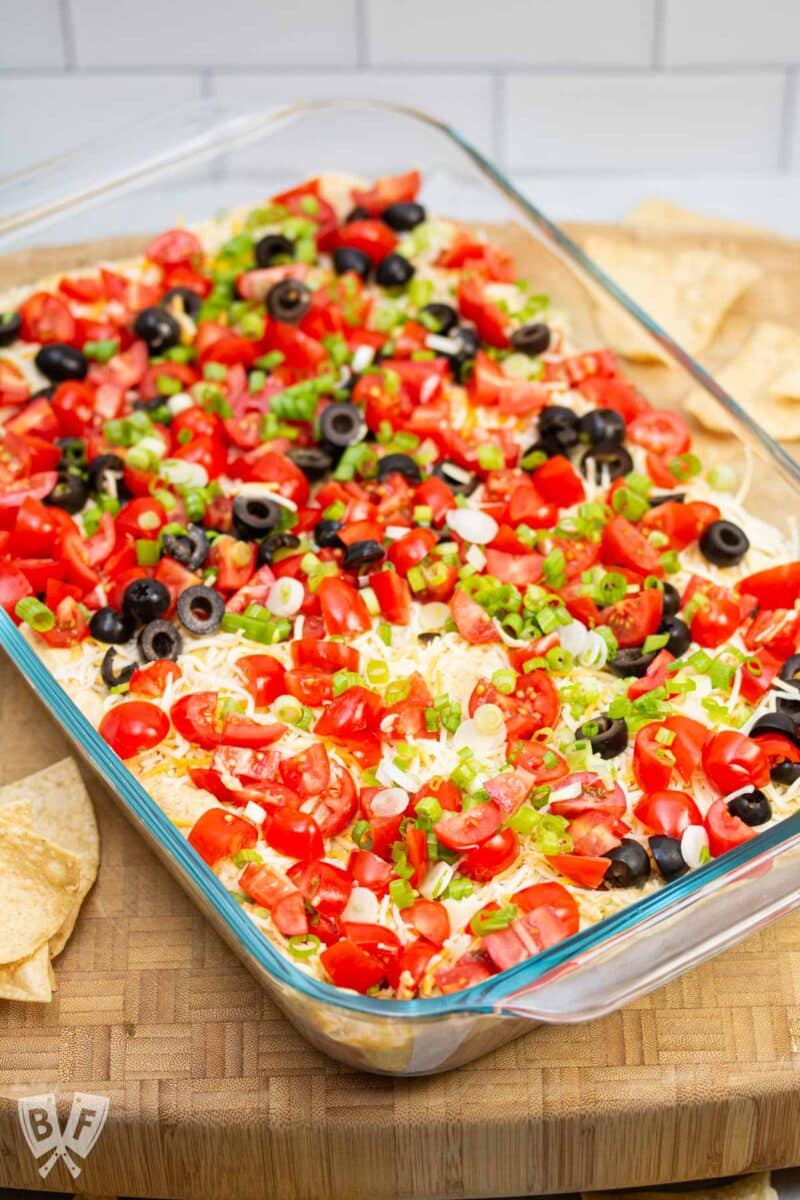 Tray of layered taco dip with olives removed from one portion.