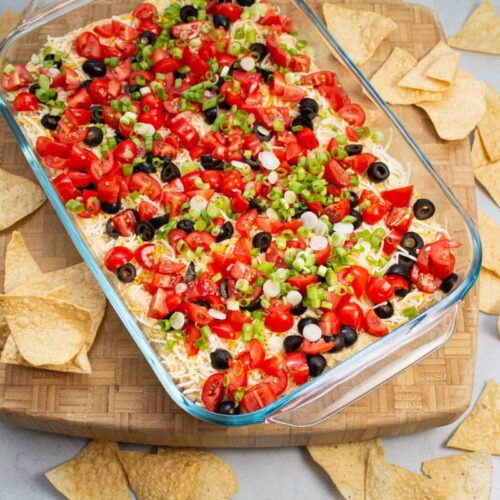 Overhead view of layered taco dip with tortilla chips alongside.