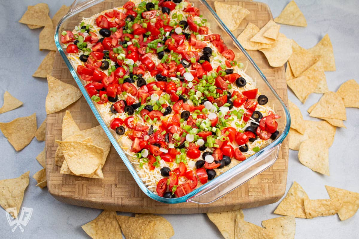 Overhead view of layered taco dip with tortilla chips alongside.