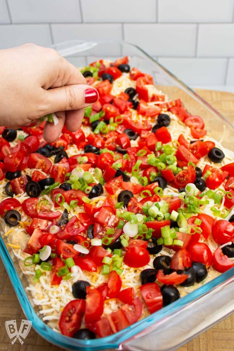 Scattering green onions on top of a layered taco dip.