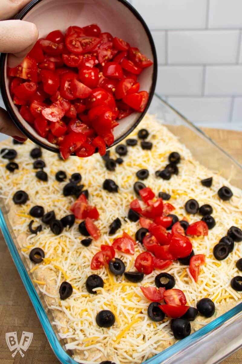 Adding tomatoes to the top of a layered taco dip.