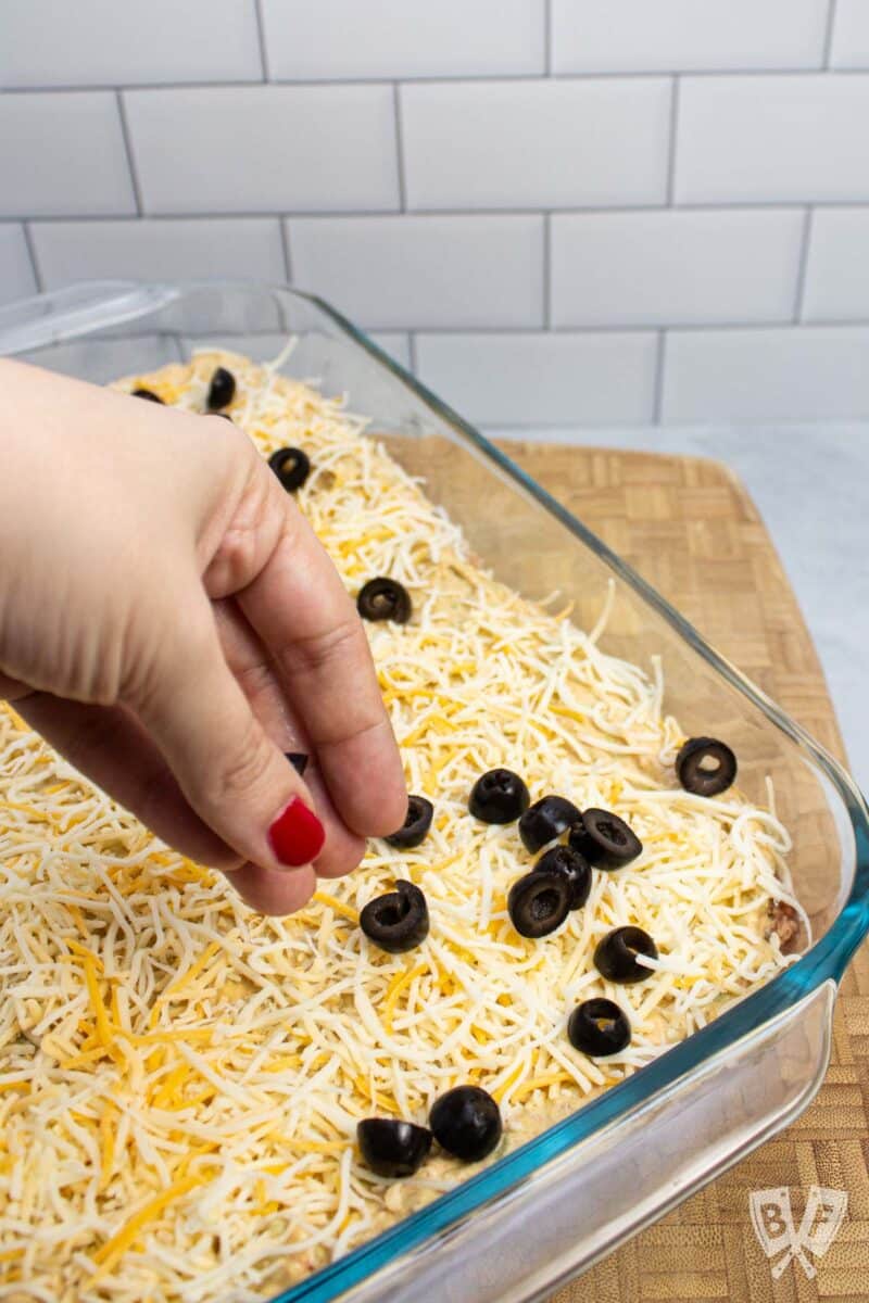 Sprinkling black olives on top of a layered taco dip.