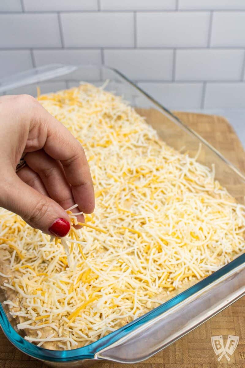 Sprinkling shredded cheese onto a layered taco dip.