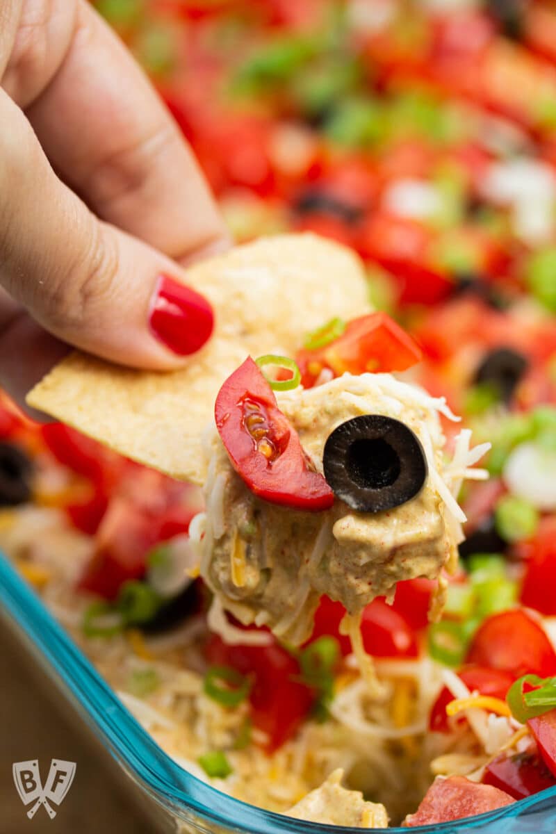 Scooping layered taco dip onto a tortilla chip.