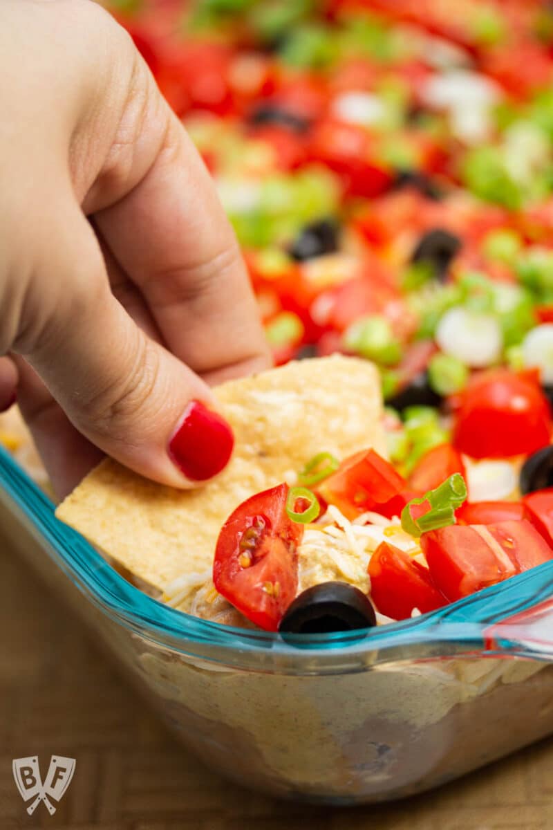 Dipping a tortilla chip into a layered taco dip.