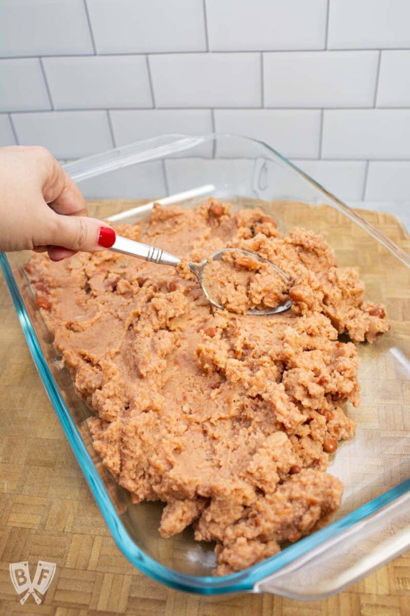 Spreading refried beans into a serving dish for layered taco dip.