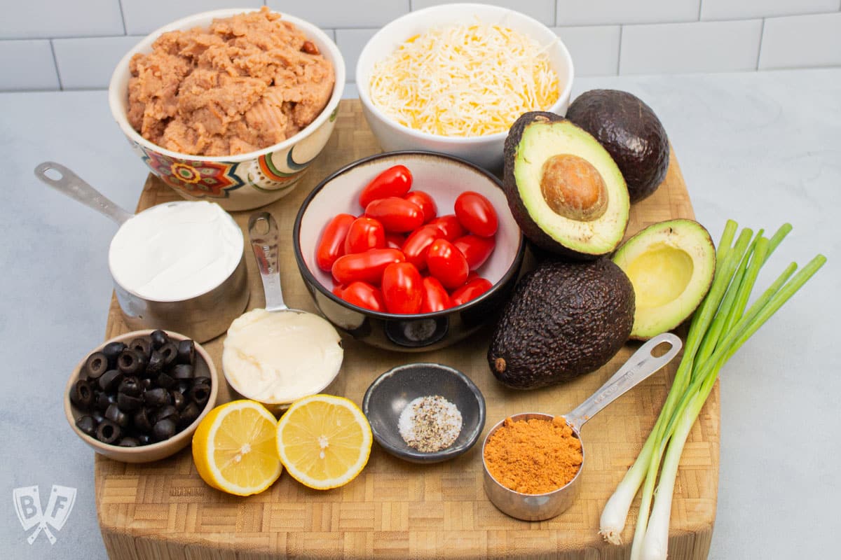 Overhead view of ingredients needed to make a layered taco dip with refried beans.