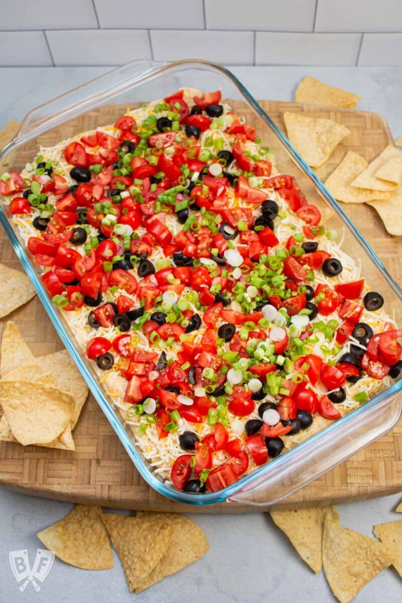 Overhead view of a layered taco dip with tortilla chips alongside.