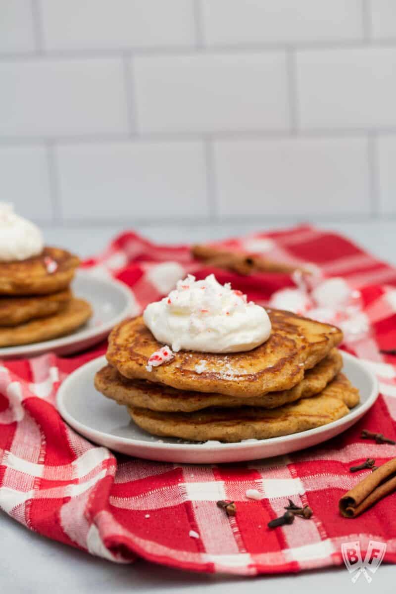 Stack of gingerbread pancakes topped with peppermint whipped cream and crushed peppermint candies.
