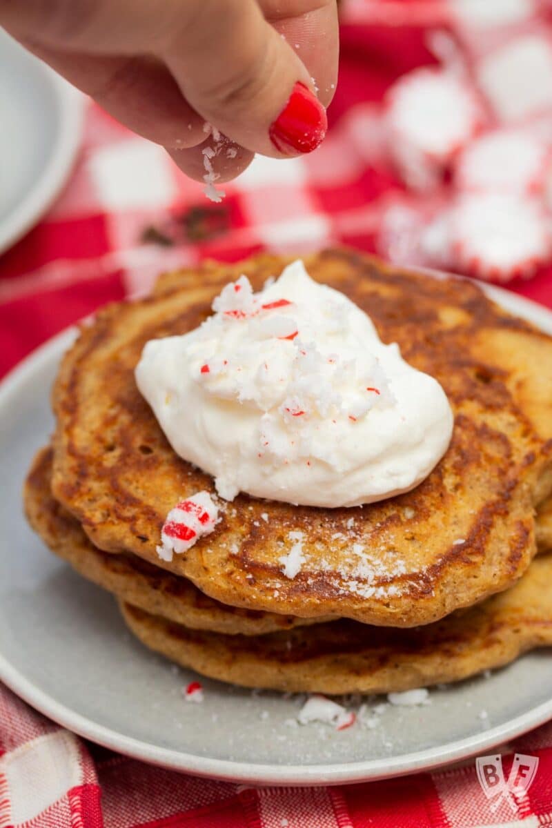 Sprinkling crushed peppermint candies onto a stack of gingerbread pancakes.