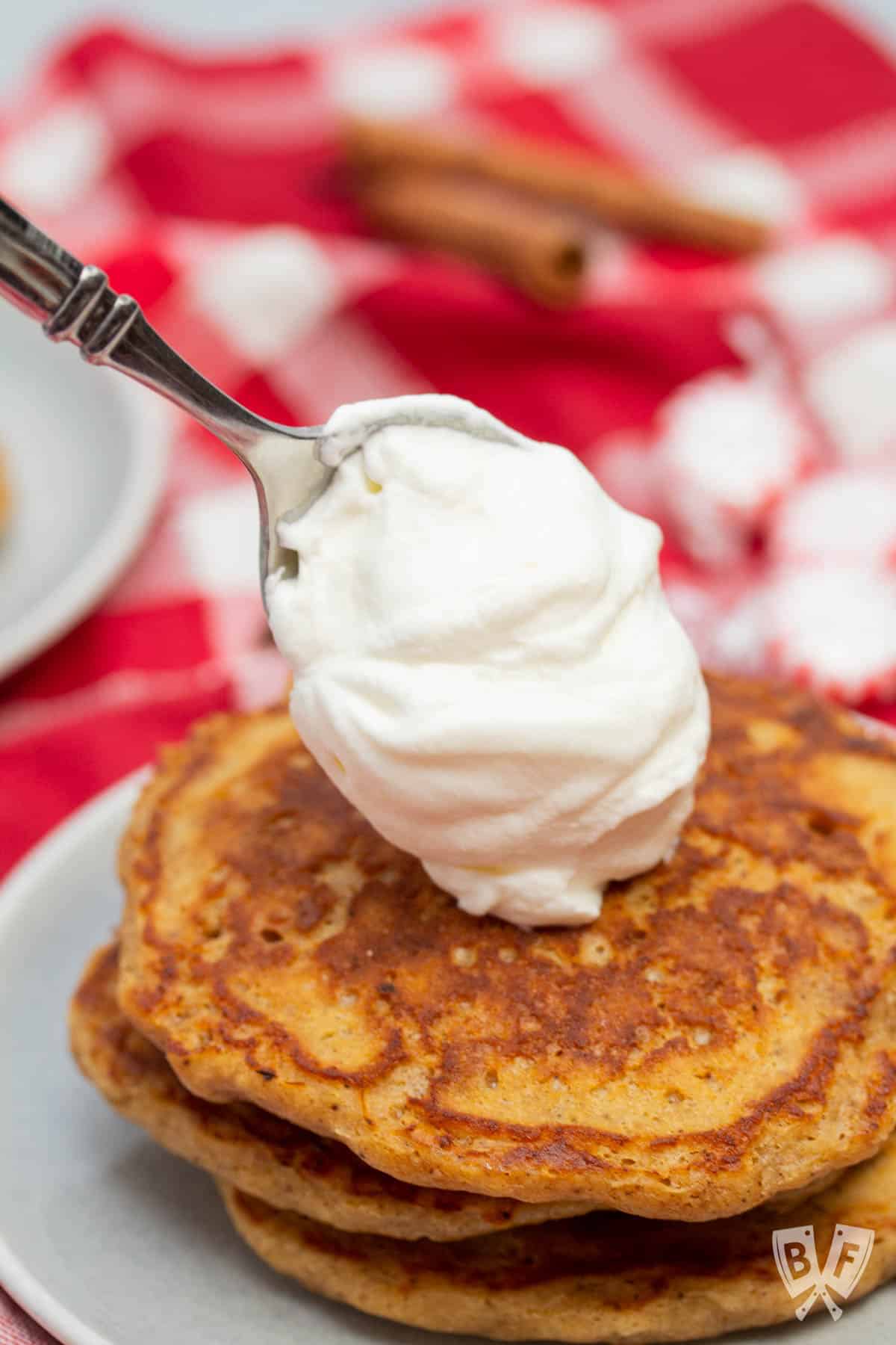 Adding a dollop of peppermint whipped cream to a stack of gingerbread pancakes.