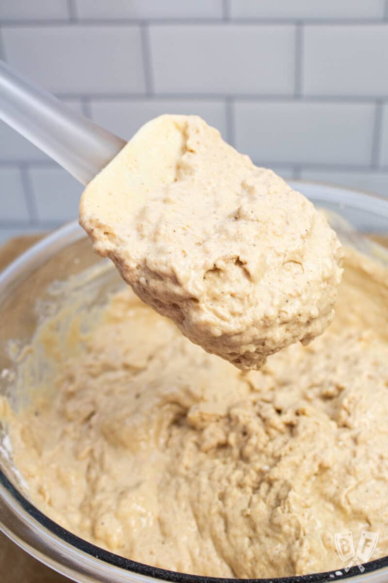 Gingerbread pancake batter in a bowl with a silicone spatula holding a scoop of batter.