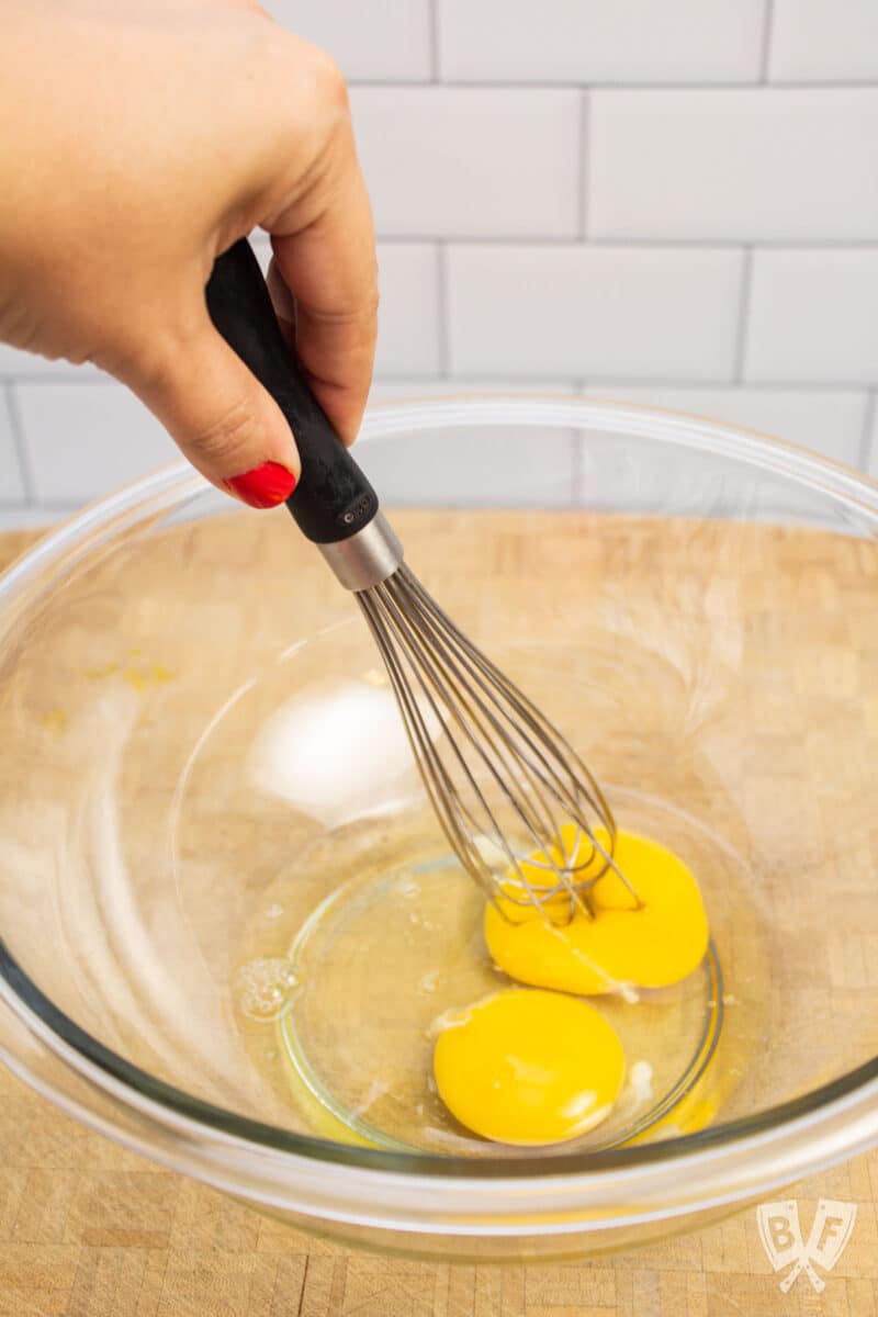 Popping the yolks of eggs in a mixing bowl with a whisk.
