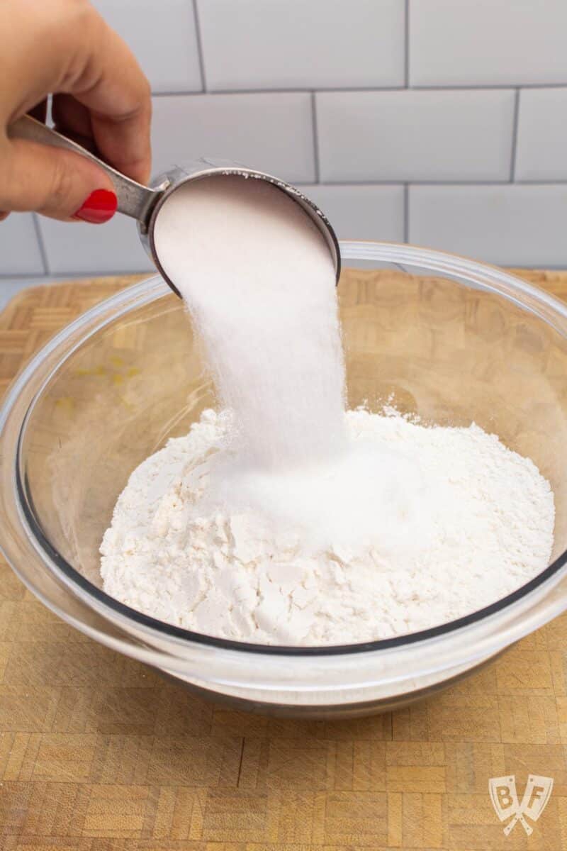 Pouring granulated sugar into a bowl of flour.