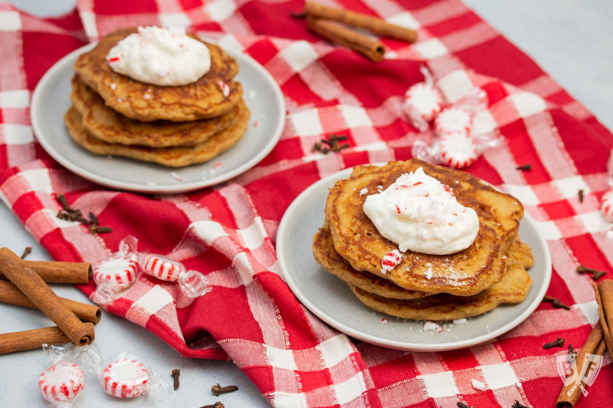 Plates stacked with gingerbread pancakes topped with peppermint whipped cream and crushed peppermint candies.