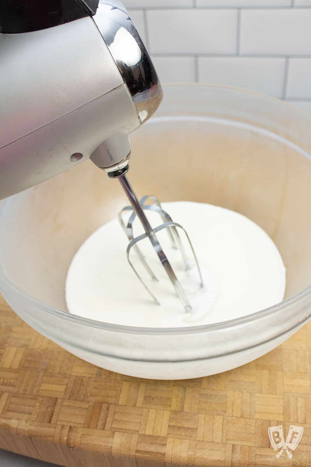 Using a hand mixer to whip cream in a bowl.