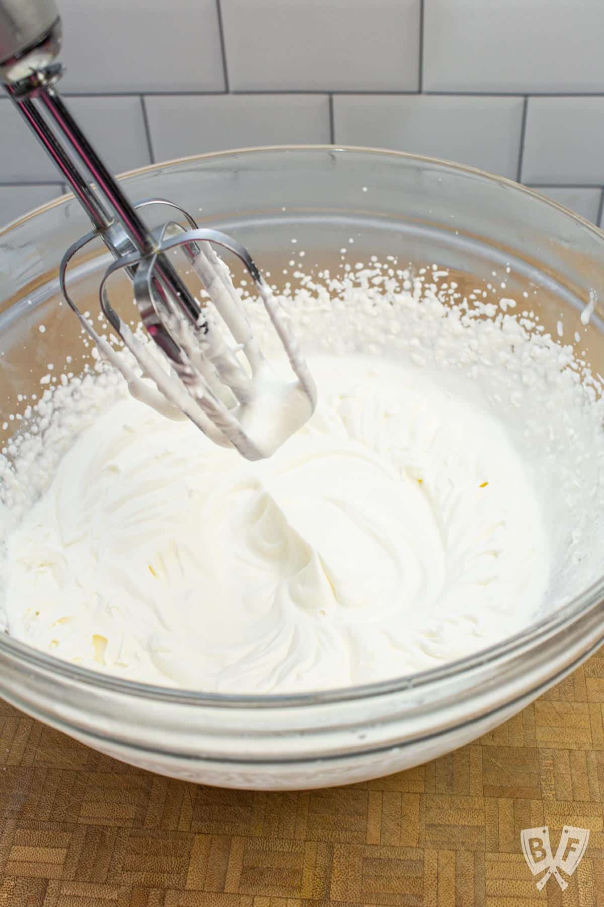 Hand mixer being lifted out of a bowl of whipped cream to show soft peaks.