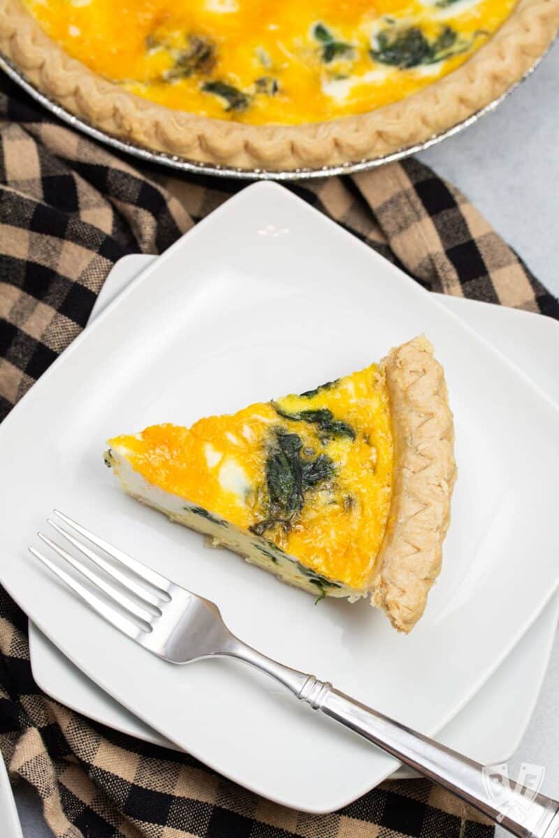 Overhead view of a slice of spinach and cheddar quiche on a plate next to the pie plate.