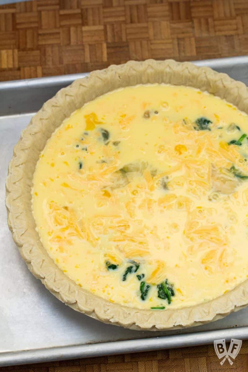 Unbaked spinach and cheddar quiche on a baking sheet ready for the oven.