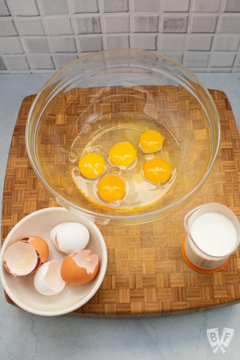 Eggs cracked into a bowl with milk alongside.
