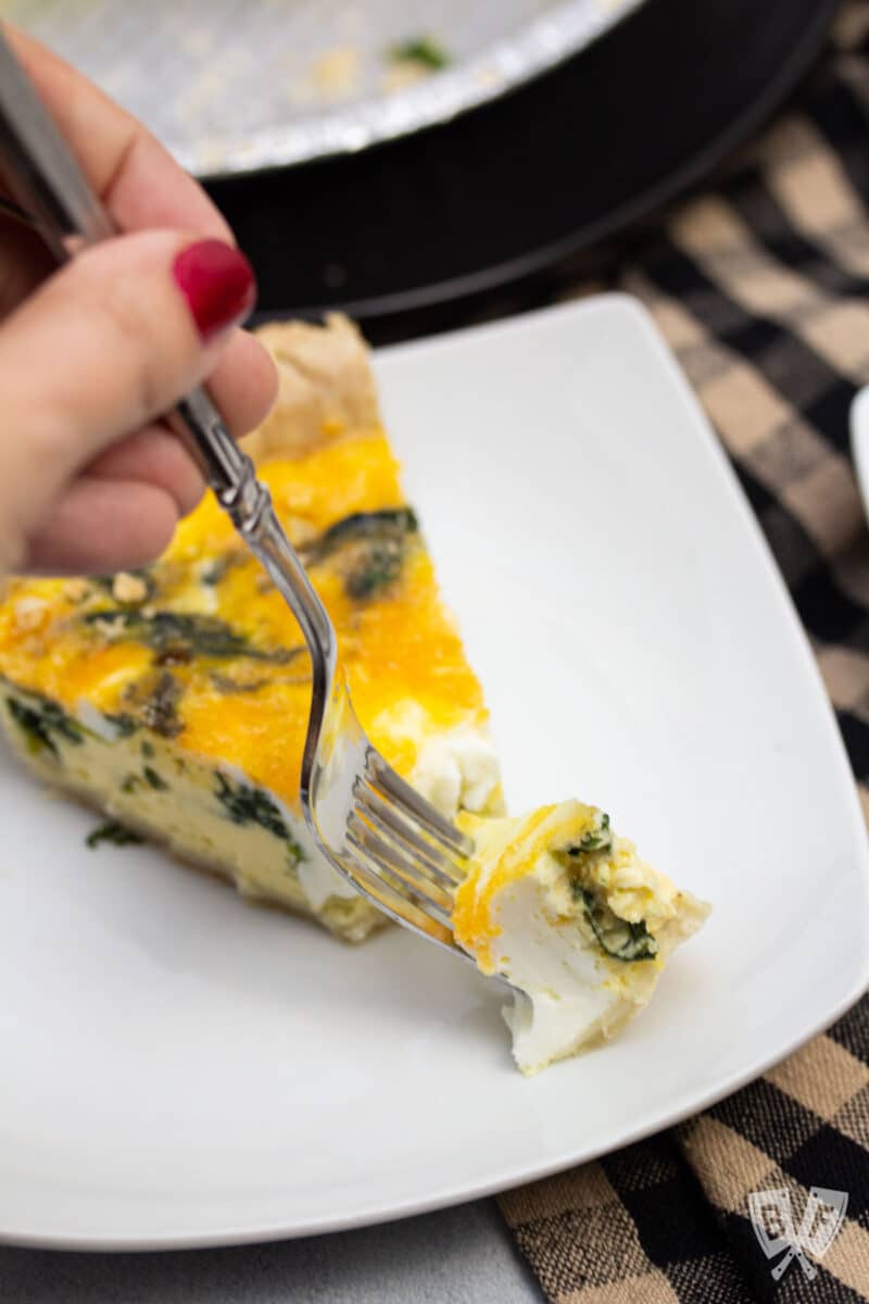 Fork grabbing a piece of spinach and cheddar quiche.