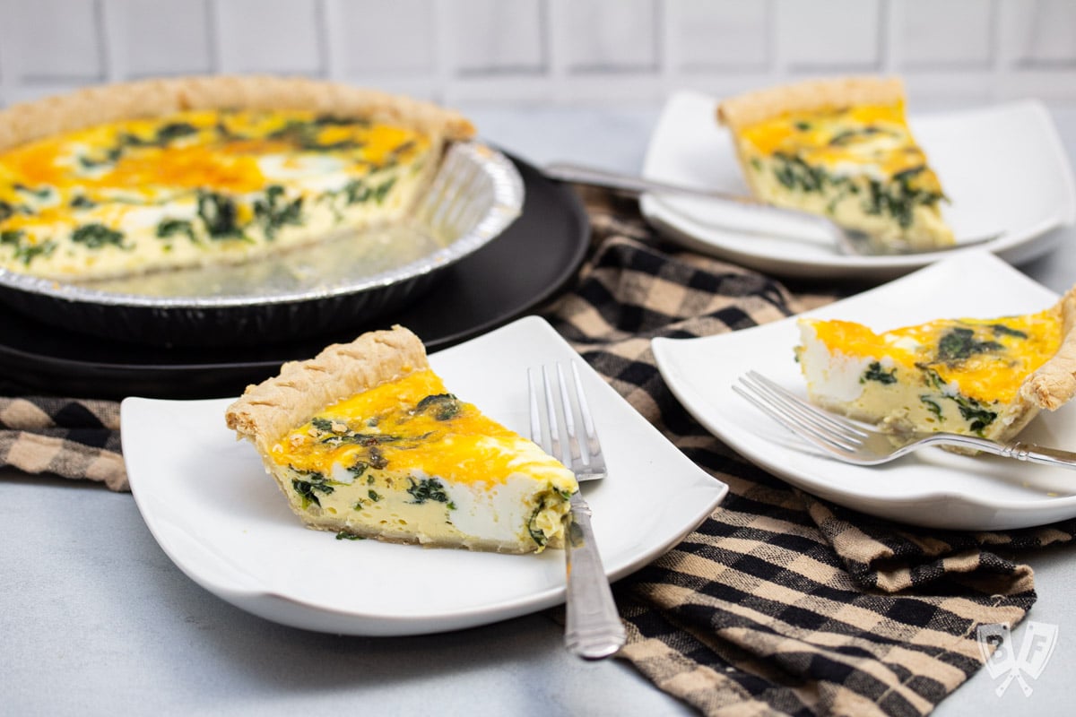 Close-up of slices of spinach and cheddar quiche on plates with forks.