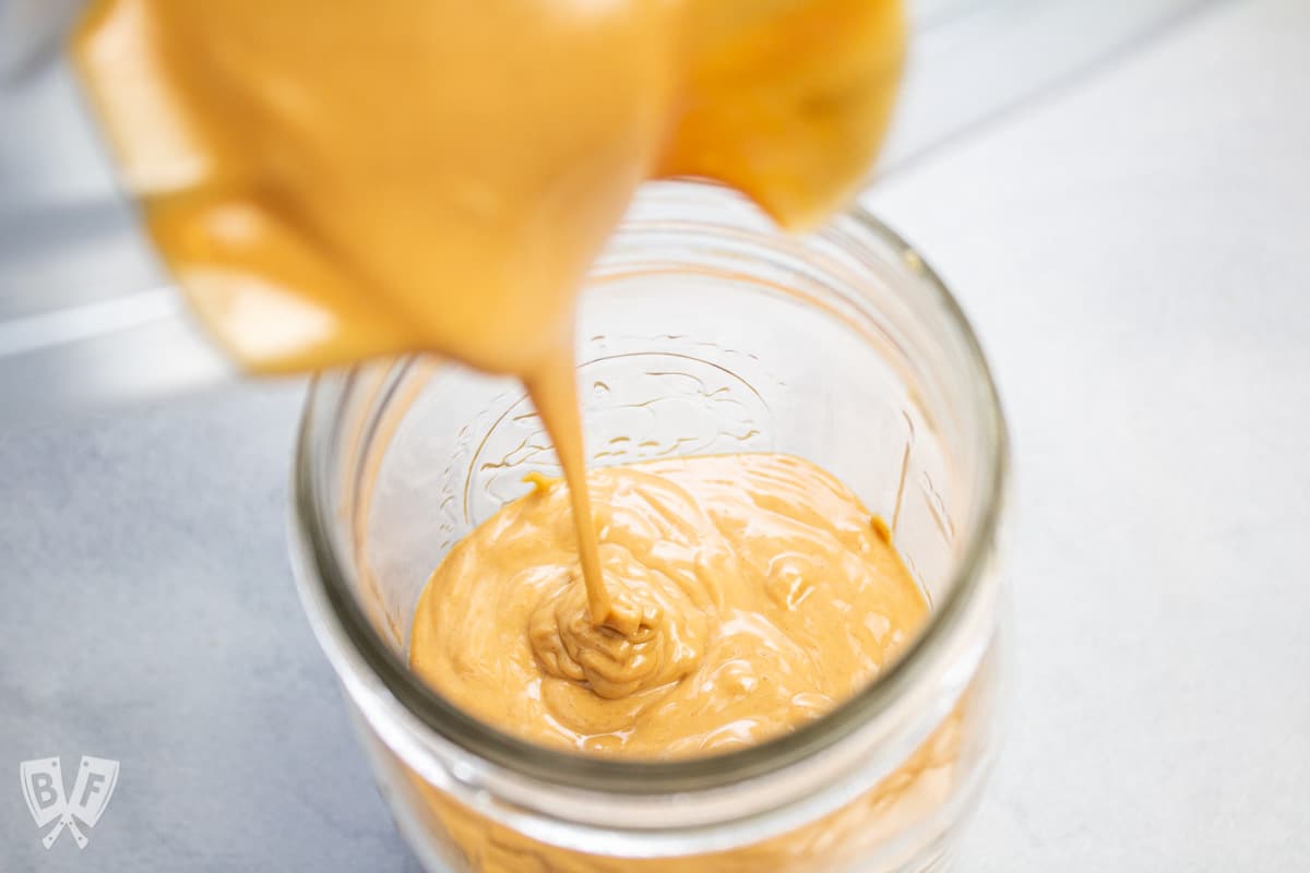 Pouring homemade peanut butter from a blender into a jar.