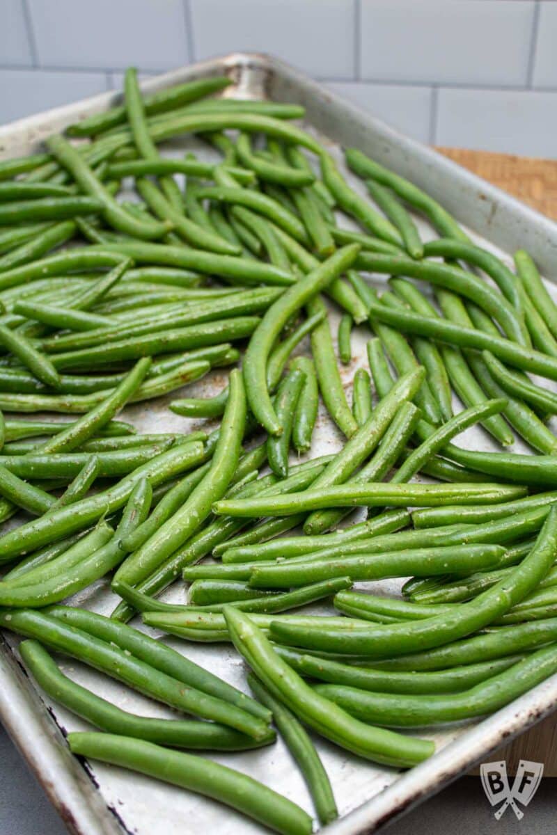 Seasoned green beans on a sheet pan ready for the oven.