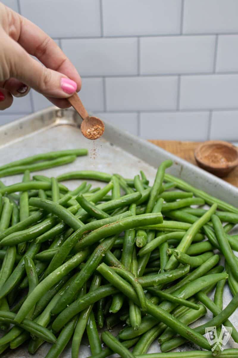 Adding grill seasoning to a sheet pan of fresh green beans.