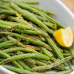 Close-up of a serving dish with roasted green beans and lemon.