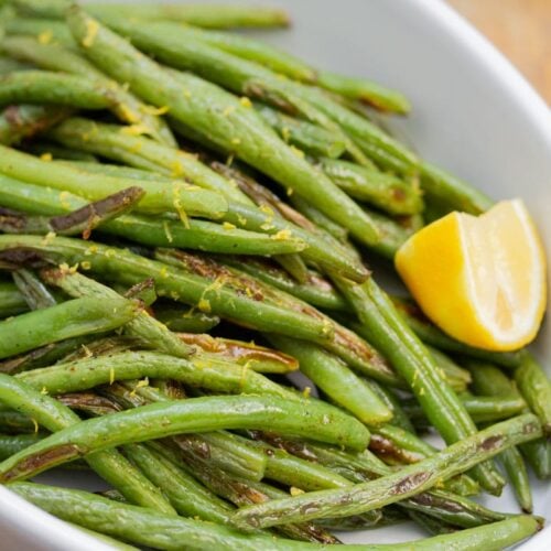 Close-up of a serving dish with roasted green beans and lemon.