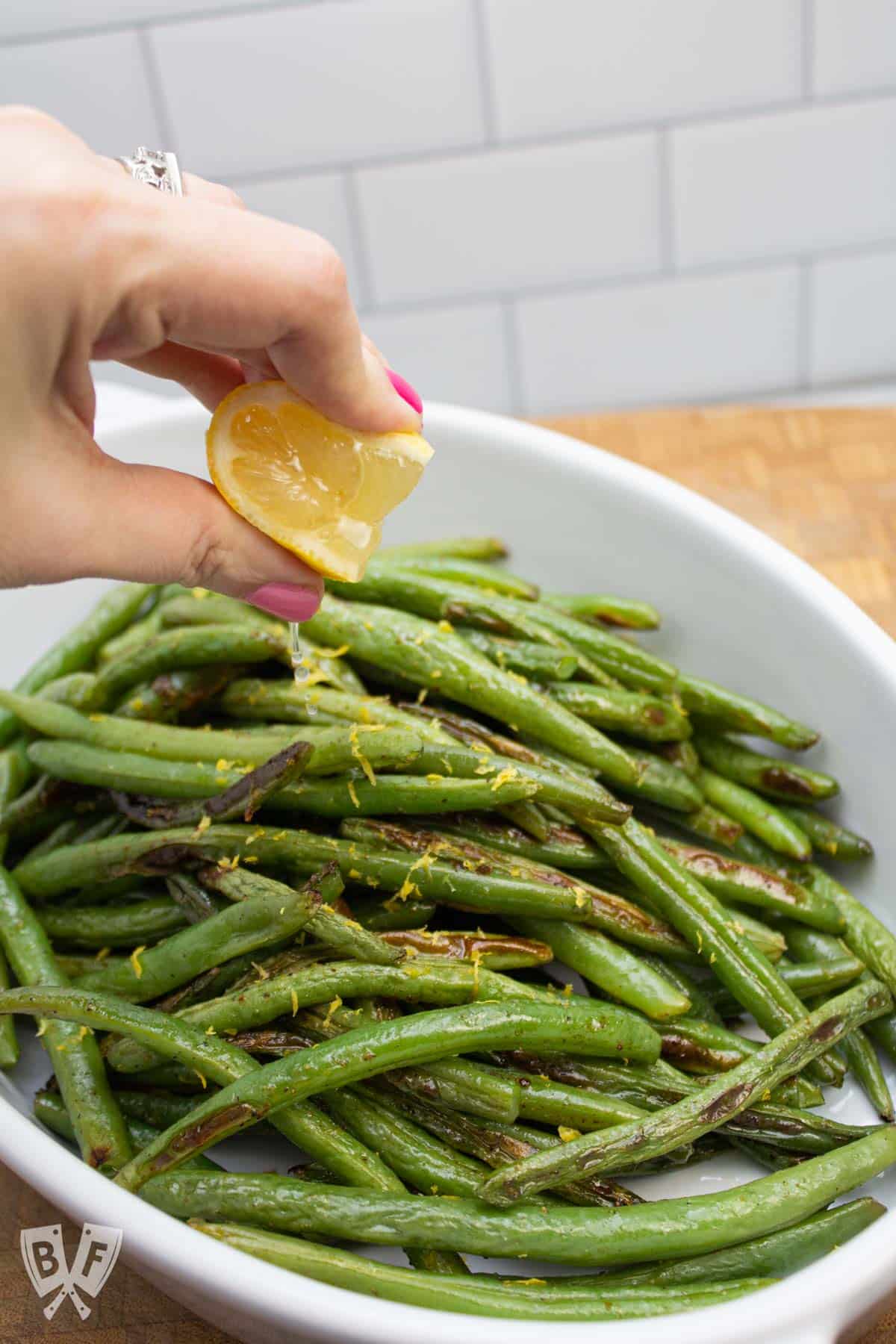Squeezing a lemon wedge over a platter of roasted green beans.
